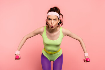 emotional sportswoman exercising with dumbbells isolated on pink