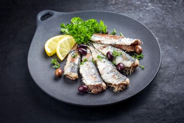 Fried sardines with lettuce and kalamata olives offered as closeup on a modern design plate with copy space