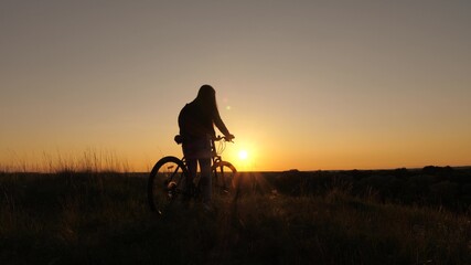 Free girl travels with bicycle at sunset. concept of adventure and travel. Hiker healthy young woman rides bicycle to edge of hill, enjoying nature and sun. lonely woman cyclist resting in park.