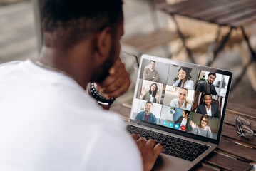 Video call. Video conference. Successful African American freelancer communicate by a video conference with his colleagues using a laptop while sitting in cafe in a summer terrace