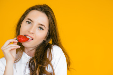 Close-up of a sexy female eating fresh strawberry. Sexual lips, red lipstick. Healthy food concept. Yellow background.