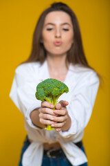 Image of cute pleased young beautiful woman posing isolated over yellow wall background holding broccoli.