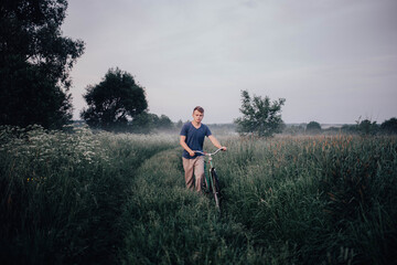 man walks with a green retro bicycle on a field road and grass in summer.