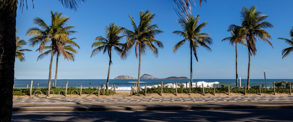 Palm trees on the boulevard of Ipanema with Portuguese tile pavement in the foreground and beach, ocean and islands out off the coast  in the background
