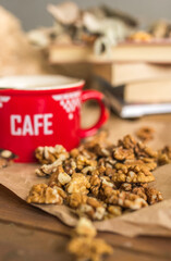 Red cup of coffee on wooden table and craft paper with books and walnuts