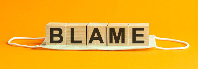 Wooden block with words blame with medical mask, health concept background, yellow background.