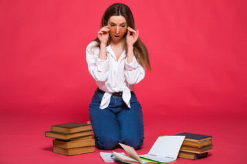 Photo of disappointed student woman using holding exercise books while sitting on floor with legs crossed isolated over pink background