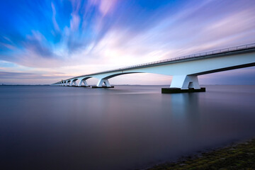 Zeeland Bridge - long white bridge over the river, beautiful blue sky with dynamic clouds. Long time, calm water of the Oosterschelde ..