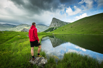 Awesome hiker in red jacket standing near mountain lake