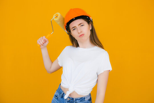 Smiling Handywoman With Hand On Hip Holding Paint Roller On Yellow Background