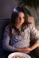 A beautiful girl with brown eyes is watching a movie in a cozy room with popcorn