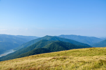 Summer landscape with meadow, green hills and reservoir under blue sky above the Ukrainian Carpathian Mountains 