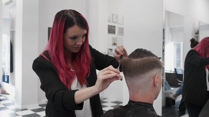 Obraz na płótnie Canvas Professional female hairstylist combing and cutting man hair