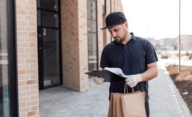 Portrait of courier with order papers and packages with food near door