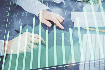 Double exposure of man's hands holding and using a phone and financial graph drawing. Analysis concept.