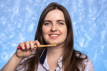  young girl with a smile holds in her hand a bamboo toothbrush in the bathroom on a blue textural background. environmentally friendly. morning hygiene concept. place for text.