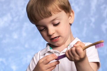 a three year old boy holds a bamboo toothbrush in his hand and examines it. eco friendly. replacing plastic with biodegradable hygiene items. European facial features.