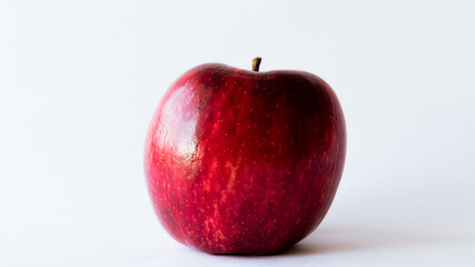 Plano frontal de una rojiza y fresca manzana completamente aislado sobre un fondo totalmente blanco con luz natural sobre ella
