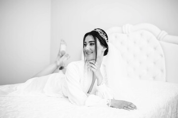 A beautiful, smiling bride in a white dress is sitting on the bed. Wedding portrait of a cheerful girl. Fashion portrait of young elegant woman in bed. Bride in the bed.
