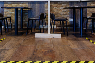 Interior low angle view of yellow and black pattern tape on the floor and temporary wooden partition in reopening restaurant for COVID-19 with New Normal and Social distancing concept.  