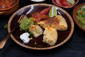 Mexican skillet cornbread served with tomato salsa and guacamole, sour cream on dark table