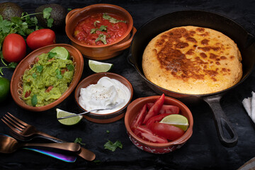 Mexican skillet cornbread served with tomato salsa and guacamole, sour cream on dark table