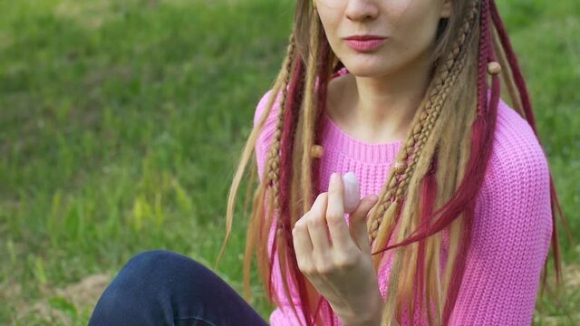Adult girl in knitted sweater and long dreadlocks is holding pink quartz yoni egg for vumfit, imbuilding or meditation outdoors on her body background outdoors