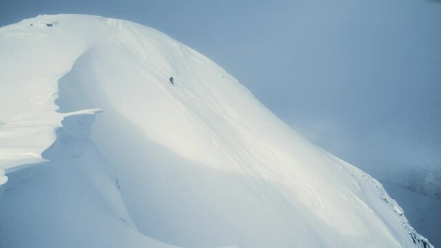 Skier drops in from the summit of a Scotish mountain in the Nevis range carving his way down the slope. Camera tracking slowly.