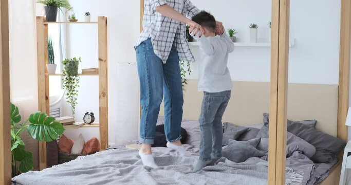Excited mother with son having fun jumping together on bed at home