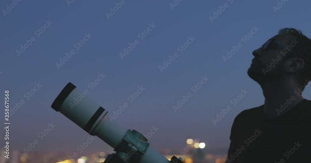 Wall mural astronomer with a telescope watching at the stars and moon with blurred city lights in the backgroun