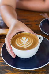 lower latte hot coffee cup with woman hand on wooden table 