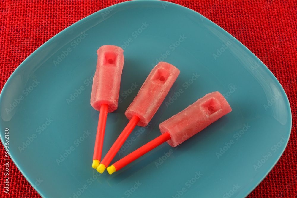 Wall mural Red strawberry whistle lollipop sucker candy on blue plate on red tablecloth