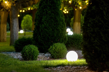 backyard light garden with lantern electric lamp with a round diffuser in the green grass with thuja bushes in a park with landscaping, closeup night scene nobody. - Powered by Adobe