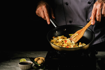 Fresh tofu near bamboo leaves, near soy sauce, , ginger and lime.The cook cuts tofu in the pan. Stirs with a wooden spoon.
