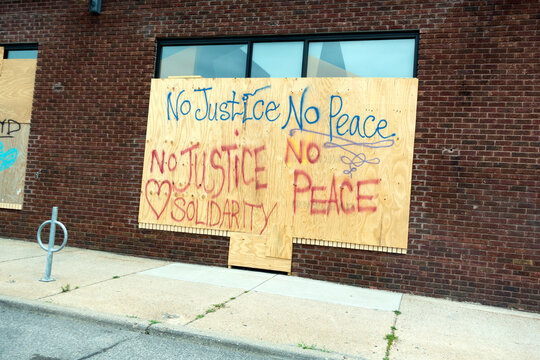Plywood protecting store windows with "No Justice No Peace Solidarity" written with bold script. Minneapolis Minnesota MN USA