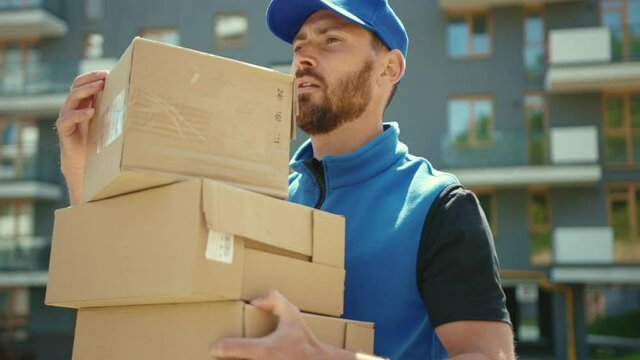 Close up tired attractive young delivery man holding cardboard box walking at street outdoor shopping package postman slow motion