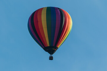 Hot air balloon in rainbow pattern blue sky copy space