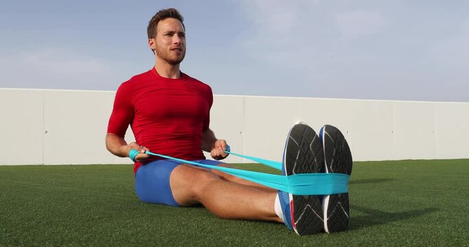 Fitness man training arms with resistance bands doing seated row exercise at outdoor gym. Body workout with equipment outside. Elastic rubber band accessory. SLOW MOTION 59.94 FPS.