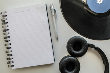 Vinyl record, notebook, pen and headphones in white table