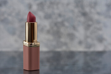 Labial color rosa sobre una superficie de marmol con un fondo de color blanco con gris y espacio...