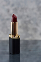 Labial color  vino con negro sobre una superficie de marmol con un fondo de color blanco con gris y...