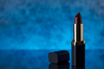 Labial color vino intenso sobre una superficie de marmol con un fondo de color azul y espacio para...
