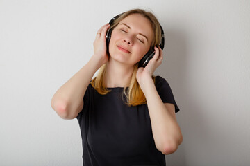 Fototapeta premium Woman at home relax and enjoy of music in headphonrs. Young blonde female listening music in earphones at home near white wall. Casual outfit. Audio rest pause at home
