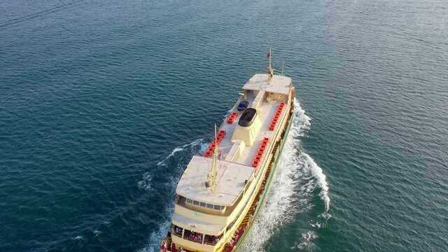 Aerial tilt up shot of passengers in ferry boat sailing on blue sea, drone flying over wake on water against clear sky - Sydney, Australia