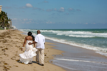African American bride and groom walking on beach