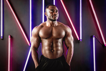 Fototapeta na wymiar African male athlete demonstrates muscles on a background of fluorescent lamps