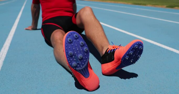 Athlete sprinter relaxing after run on athletics running track and field stadium. Close up of spike running shoes on man track runner resting after sprint training outdoors. Fitness and sports.