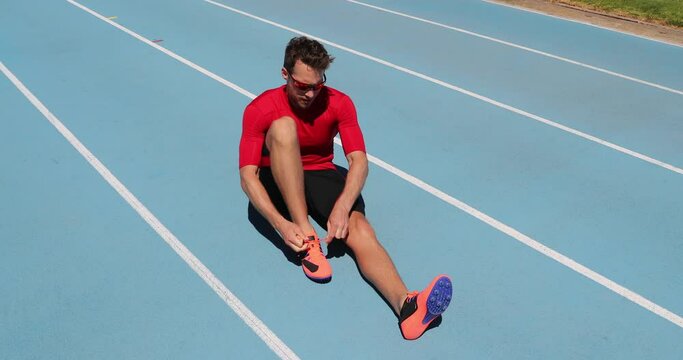Athlete sprinter getting ready to run tying shoe laces on stadium running tracks. Man track runner preparing for race marathon training outdoors. Fitness and athletics sports.