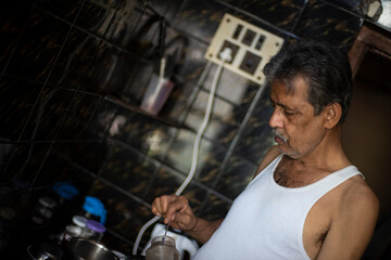 Old/aged Indian Bengali man with beard is making tea in his kitchen wearing casual dress. Indian lifestyle and seniors