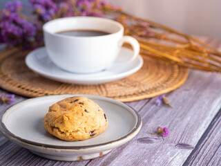 Close-up of a cookie on a plate with a white coffee cup and flower blurred background. Space for text.